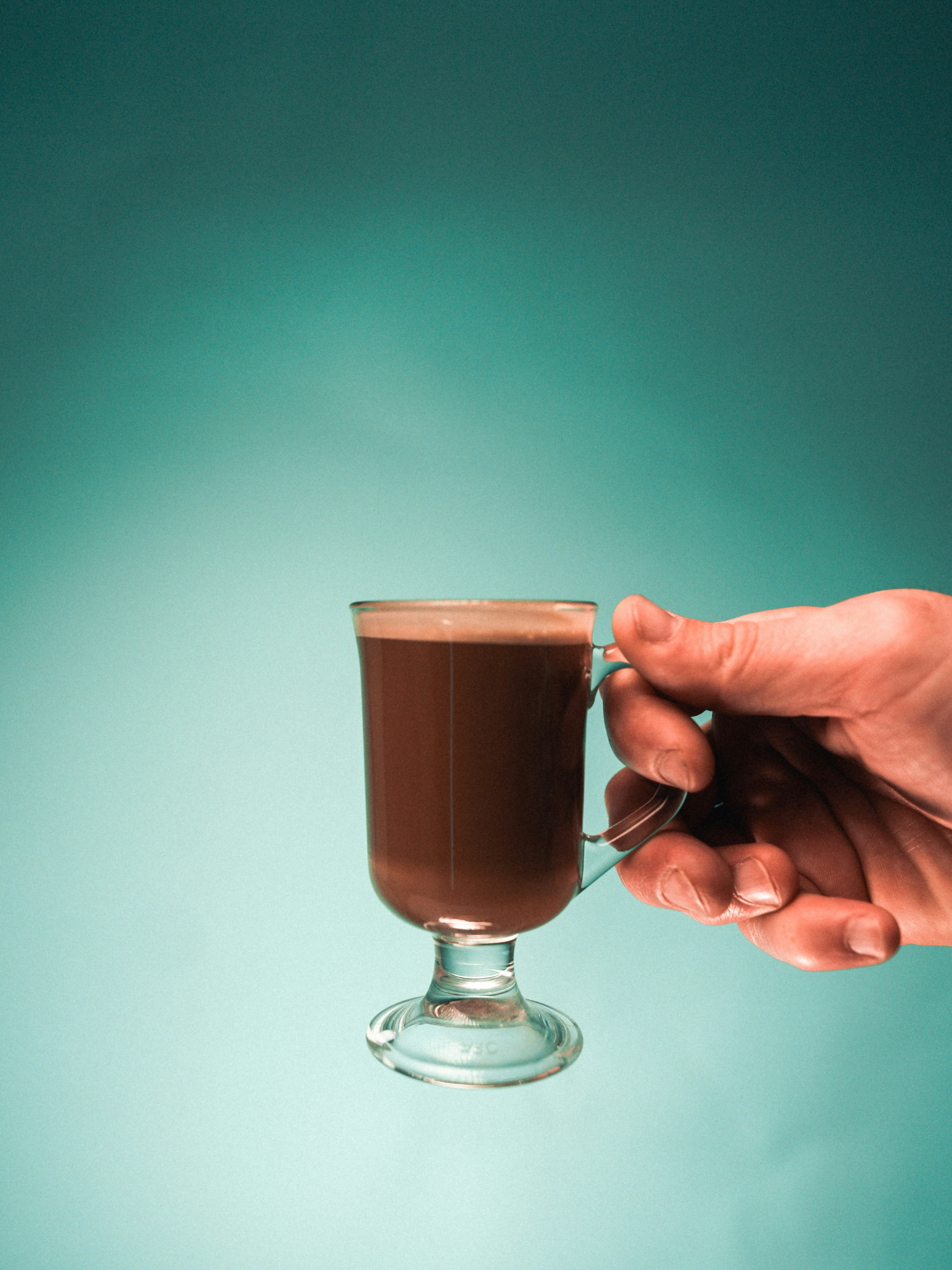 person holding clear glass cup with brown liquid